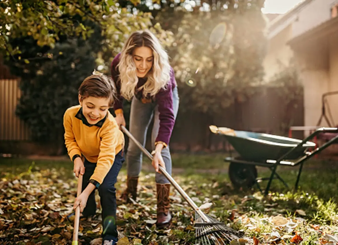 A mother and a son raking leaves in the backyard