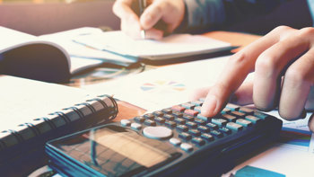 Person pressing button on calculator and writing in notepad