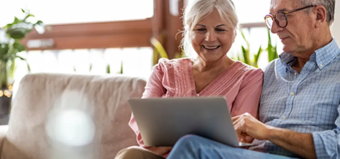 A senior couple sitting on a couch and looking at a laptop screen together