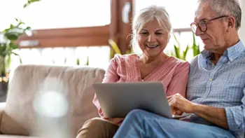 A senior couple sitting on a couch and looking at a laptop screen together