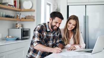 A happy couple filling out a paper at their kitchen table