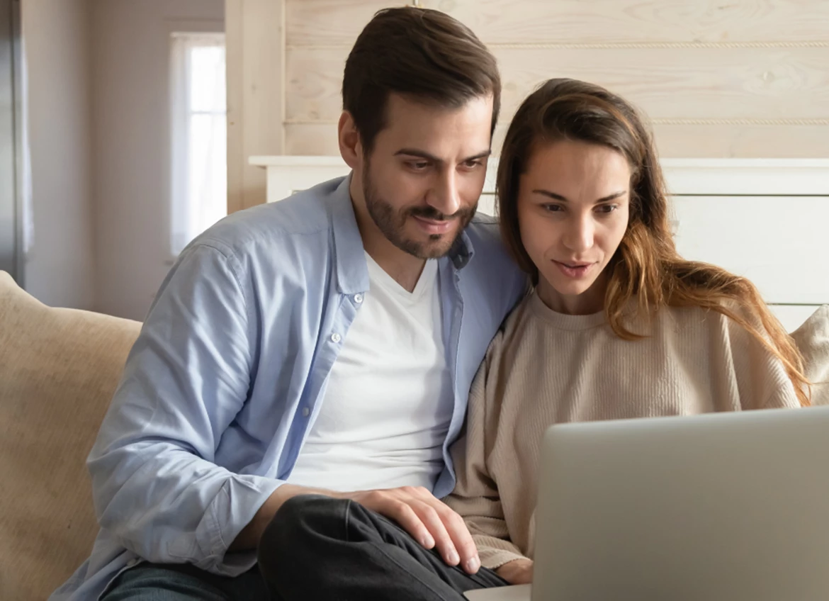 A couple sitting comfortably on a couch and looking at the laptop together