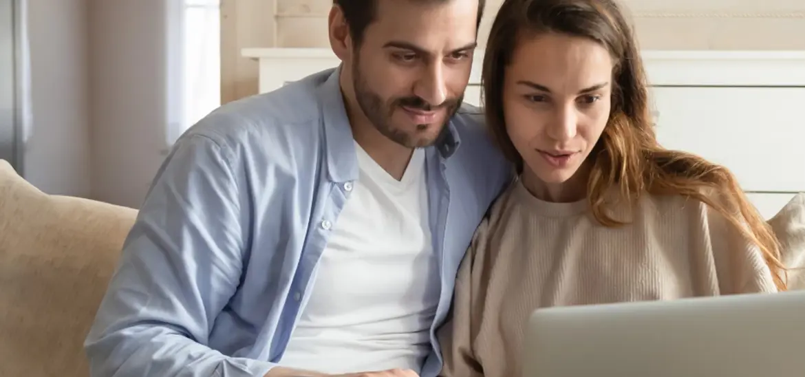 A couple sitting comfortably on a couch and looking at the laptop together